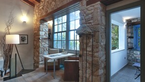 A room with stone walls, a wooden ceiling, a table with chairs, a floor lamp, and a window with a view of greenery. - Live in the Acropolis' Shadow-now w/ super Terrace
 (Athina)