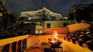 A terrace with a fire pit, a chair, and a view of a castle-like structure in the background. - Live in the Acropolis' Shadow-now w/ super Terrace
 (Athina)