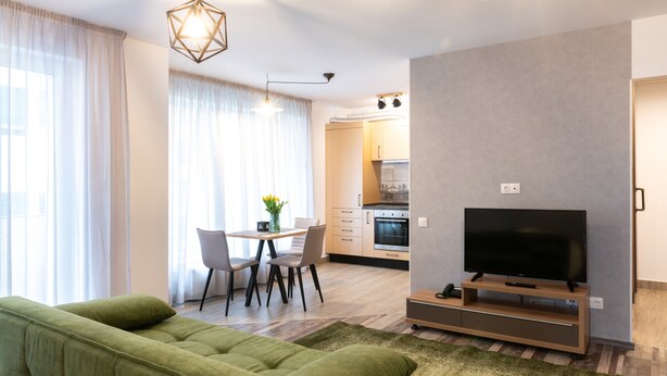 Een moderne woonkamer met een groene bank, een flatscreen televisie en een eethoek met een tafel en stoelen.