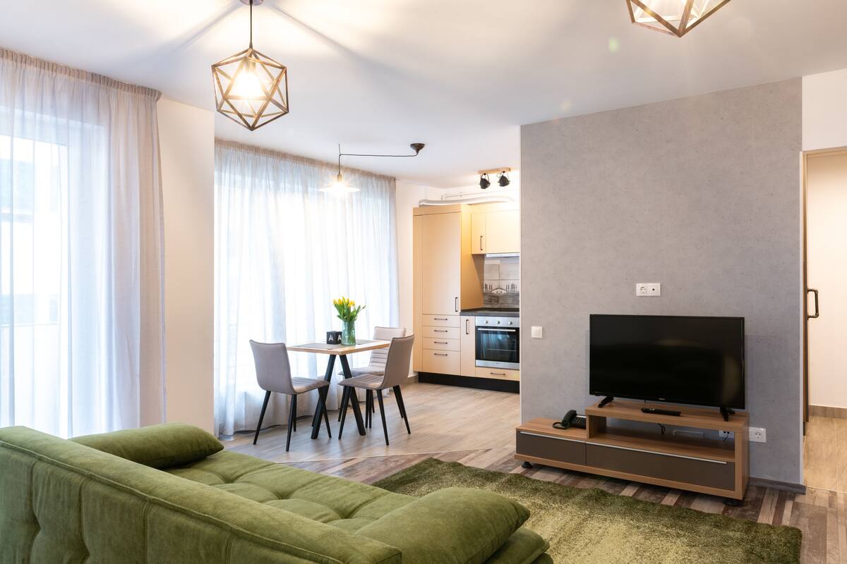 Uma sala de estar moderna com um sofá verde, uma TV de tela plana e um espaço de jantar com uma mesa e cadeiras.