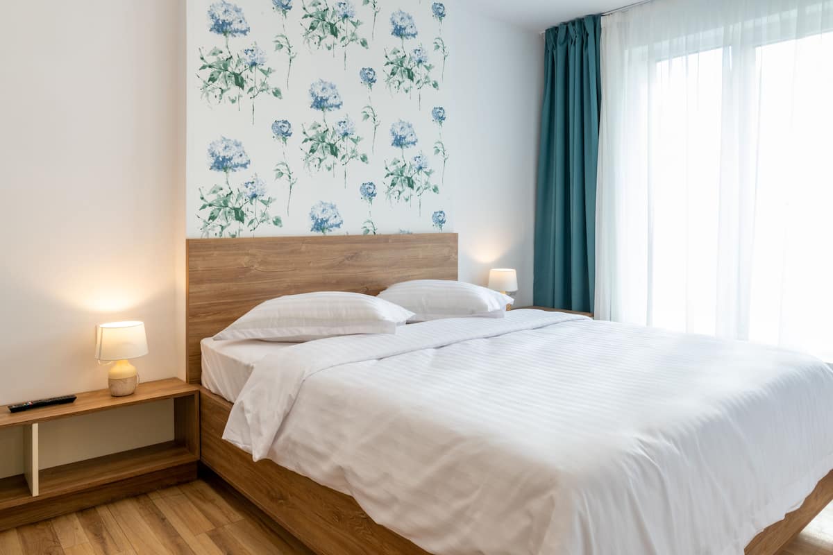 Uma cama bem arrumada com lençóis brancos, uma cabeceira de madeira e uma mesa de cabeceira com abajur.