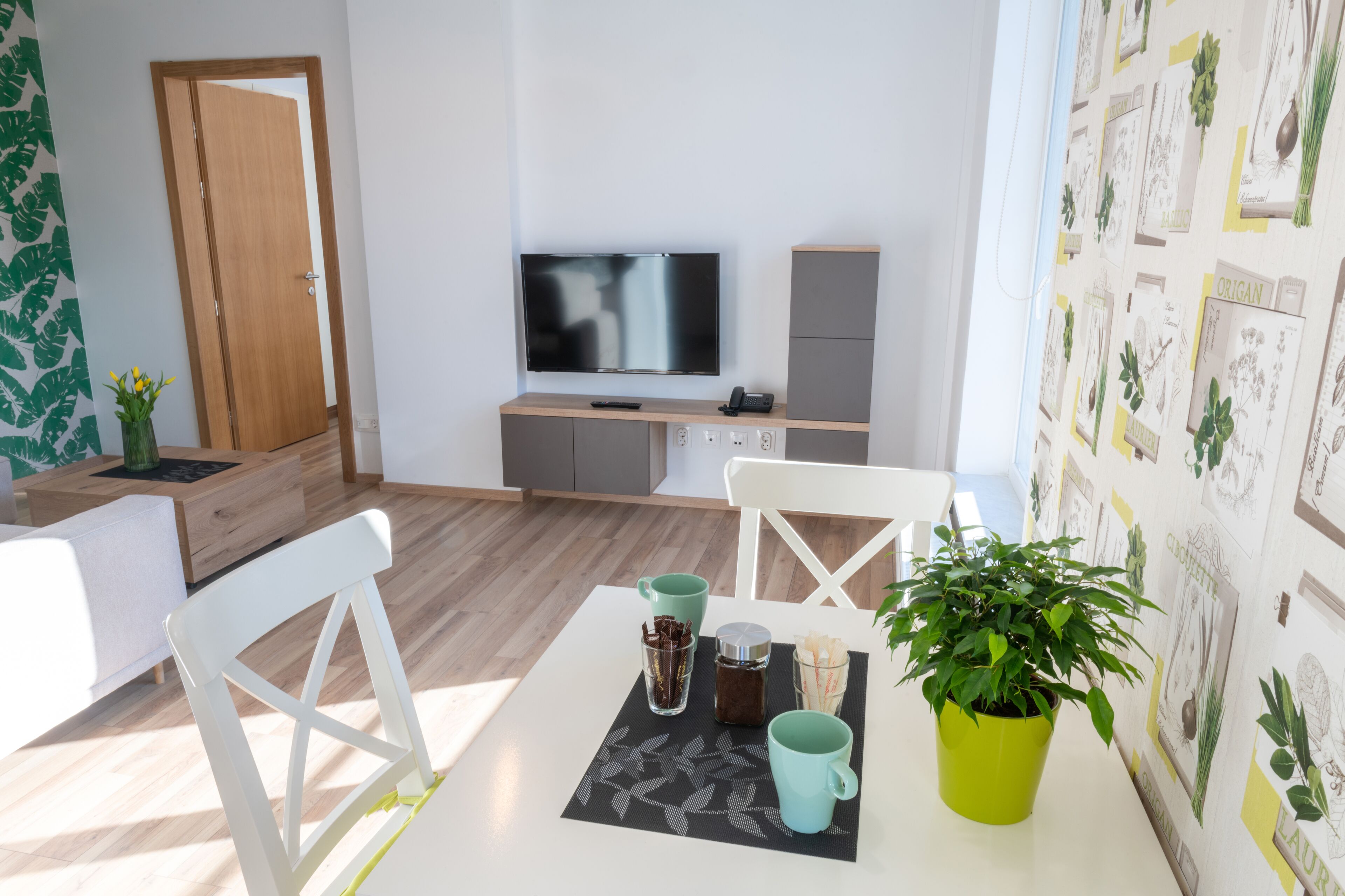 Una sala moderna con televisor de pantalla plana, una puerta de madera y un comedor con mesa, sillas y una planta en maceta.