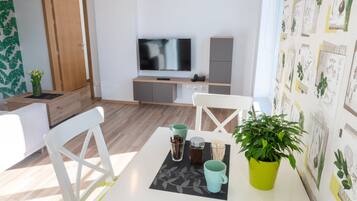 Una sala moderna con televisor de pantalla plana, una puerta de madera y un comedor con mesa, sillas y una planta en maceta.