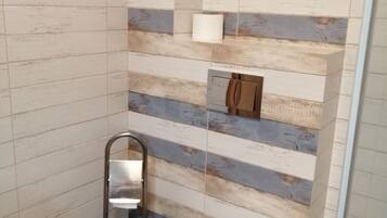 A modern bathroom with a striped tile wall, a toilet, a handrail, and a small shelf with a tissue box.