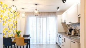 Een moderne keuken met een eethoek, met een behang, hanglampen en een groot raam met dunne gordijnen.