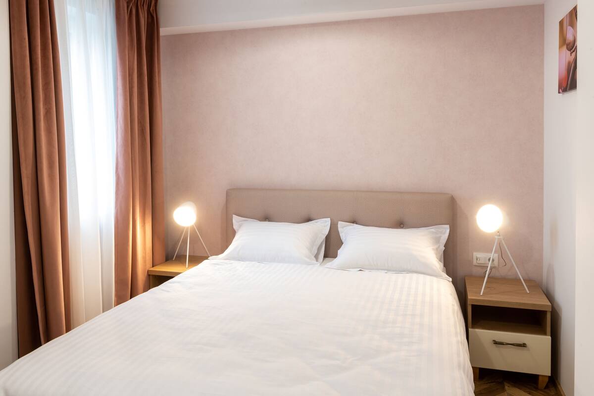 Uma cama bem arrumada com duas mesas de cabeceira, cada uma com uma luminária.
