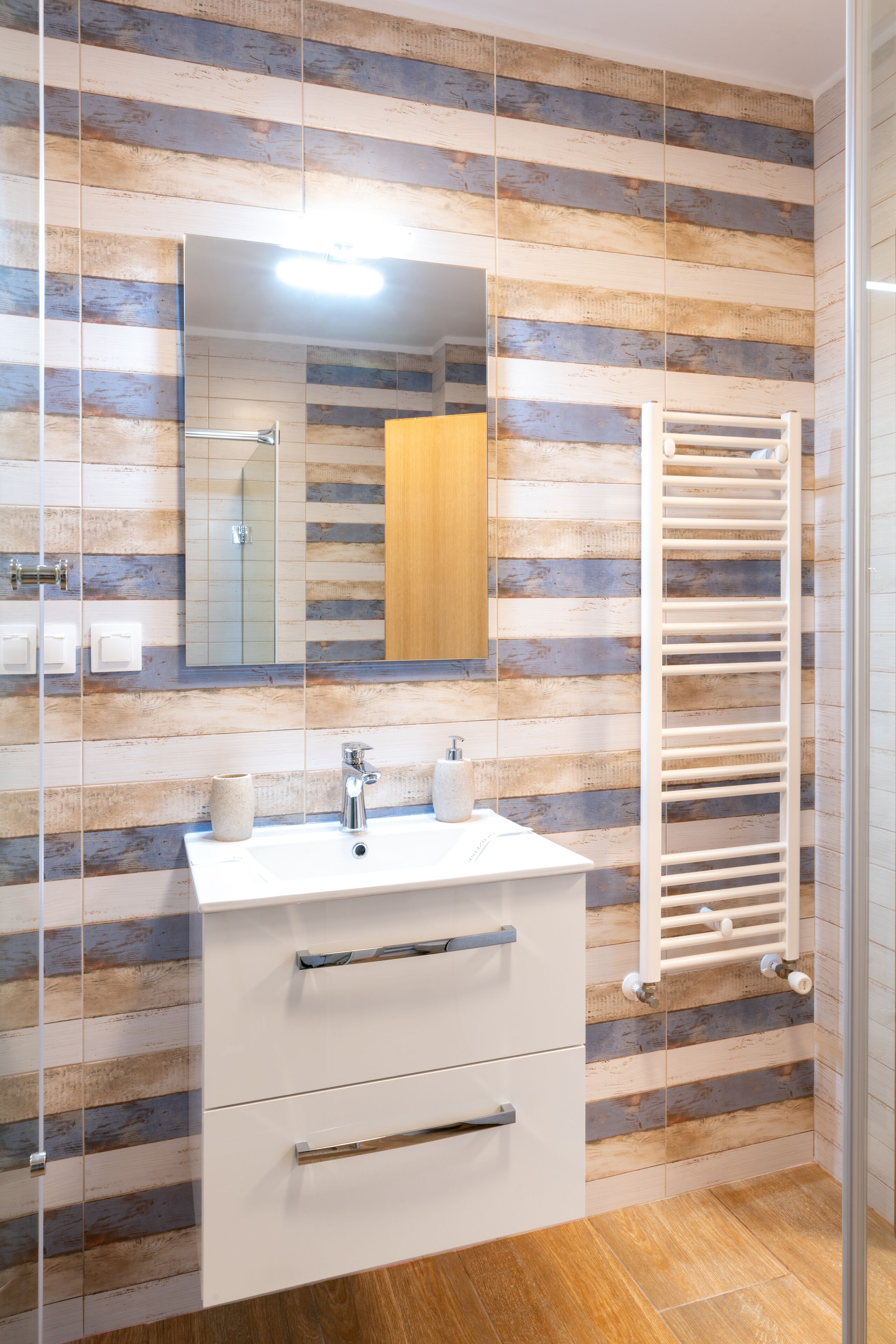 A bathroom with a wooden plank wall, a white sink, a mirror, and a towel rack.