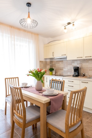 A dining area with a table set for four, wooden chairs, a vase with flowers, and a coffee maker on the counter. - TCI Apartments (Cluj-Napoca)