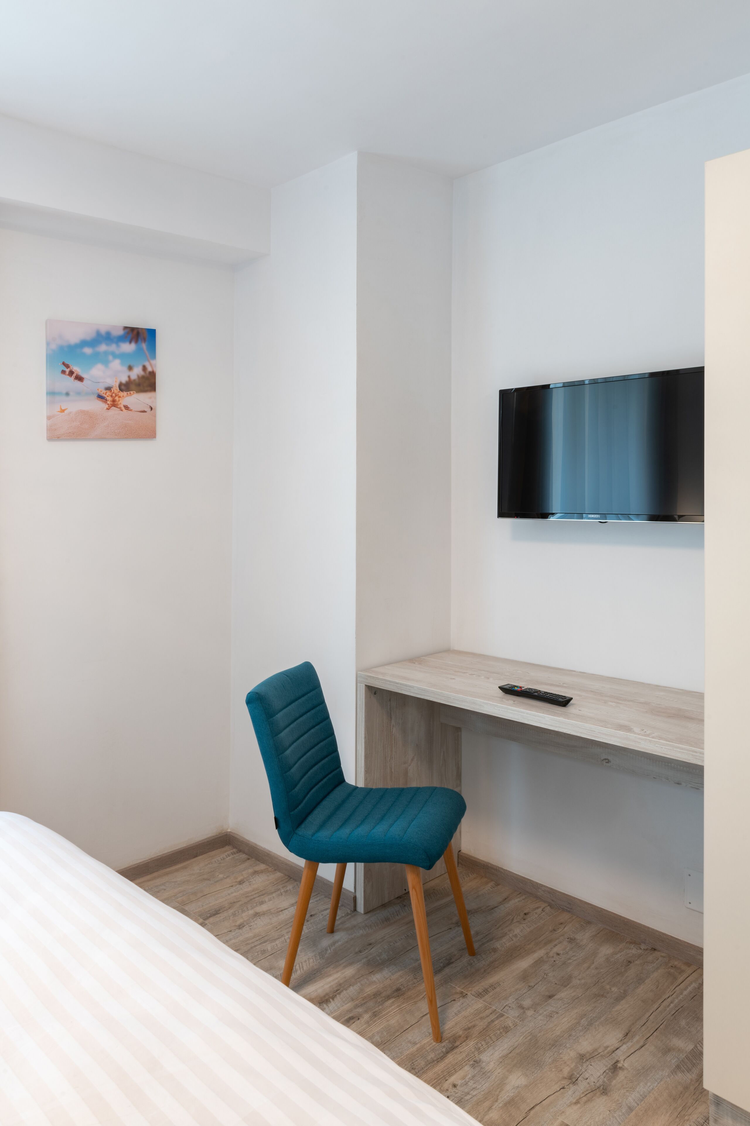 A modern room with a bed, a blue chair, a TV mounted on the wall, and a painting on the wall.