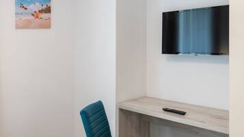 A modern room with a bed, a blue chair, a TV mounted on the wall, and a painting on the wall.