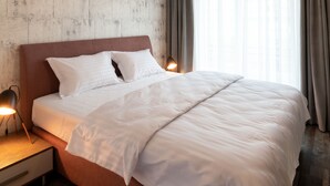 Een keurig opgemaakt bed met witte lakens, een houten hoofdbord en een nachtkastje met een lamp.
