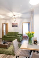 Una sala de estar moderna con un sofá verde, una mesa de centro de madera y una mesa de comedor con sillas. Hay un jarrón con flores amarillas sobre la mesa de comedor.