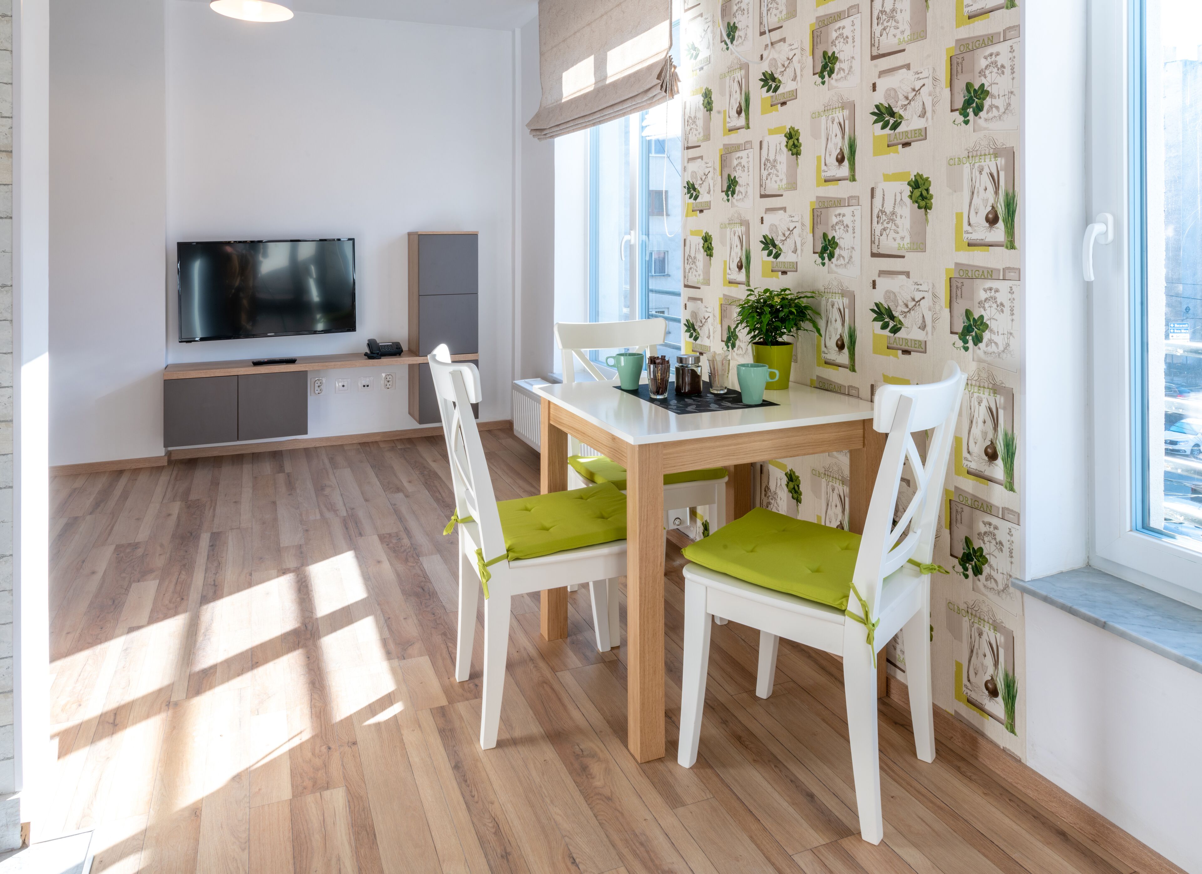Eine moderne Küche mit Essbereich, Holzboden, weißen Schränken, einem Flachbildfernseher und einem Fenster mit Blick auf die Stadt.