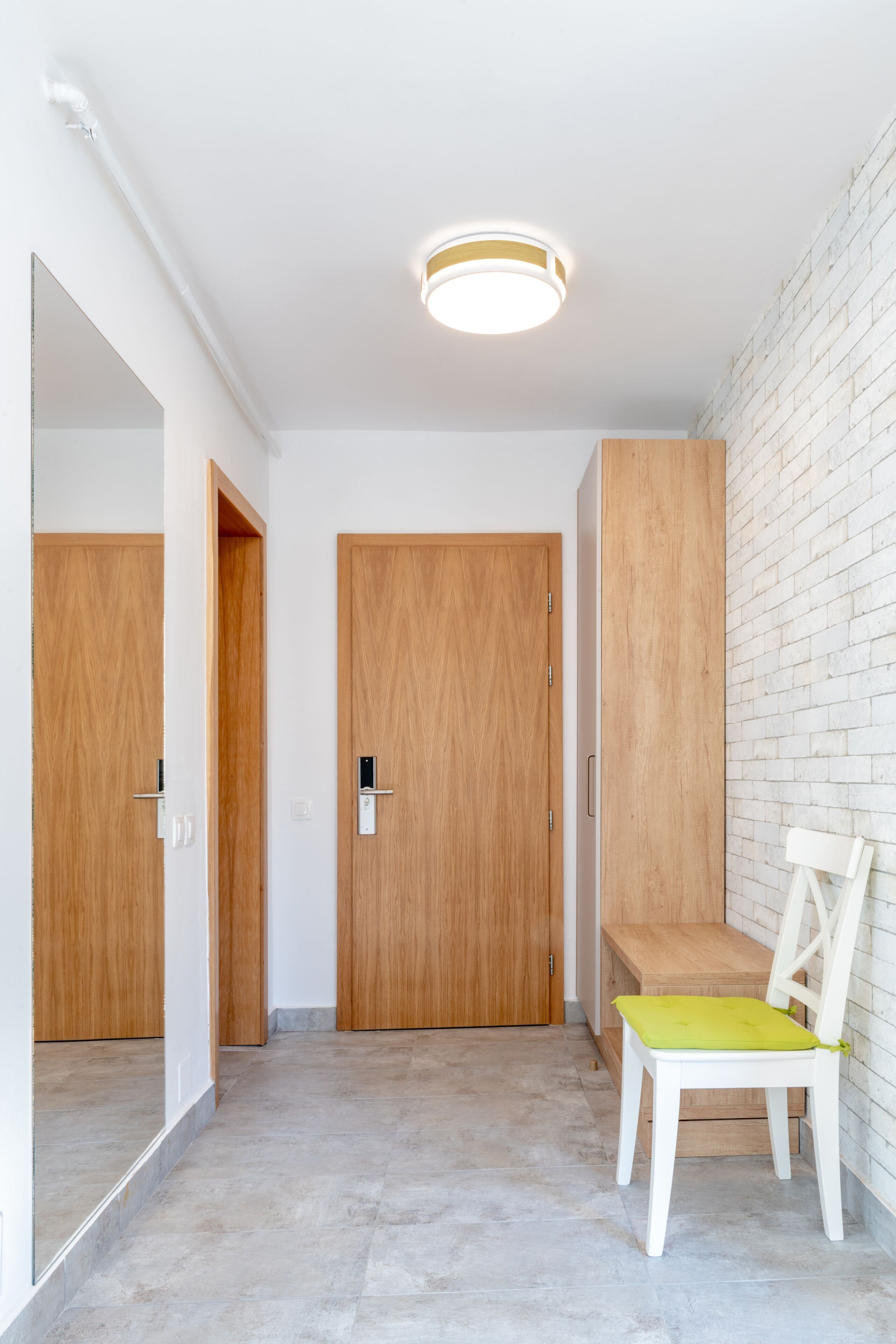 A hallway with wooden doors, a bench, and a white brick wall.
