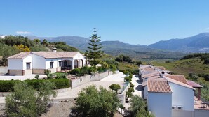 A white villa with a tiled roof, surrounded by greenery and hills in the background. - House in Huetor, Rural Tourism, Beach & Pool (Vinuela)
