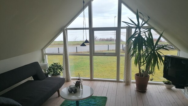 Ett modernt sovrum i loftstil med ett stort takfönster, en soffa, ett litet runt bord och en tv.