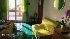 Una habitación con una cama, un sofá, una silla, una mesita, una planta en maceta y un espejo en la pared.