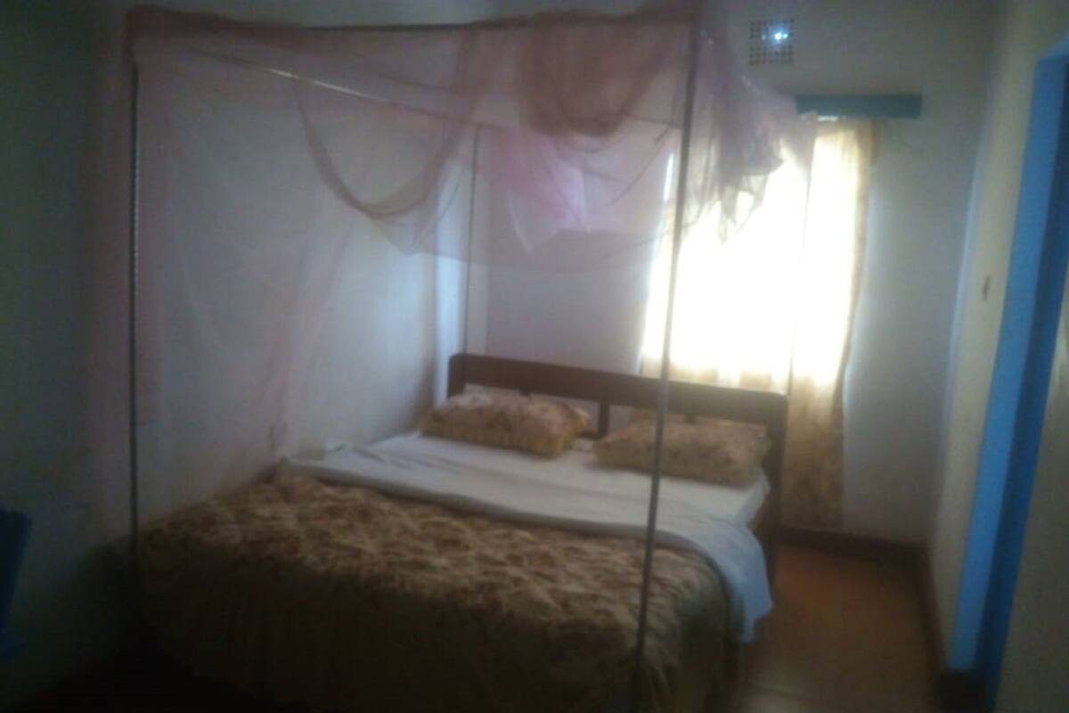 A single bed with a mosquito net, a wooden headboard, and a white bedspread.