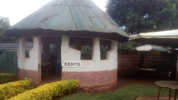 En liten, envåningsbyggnad med ett halmtak, där ordet ”KENYA” är skrivet på sidan.