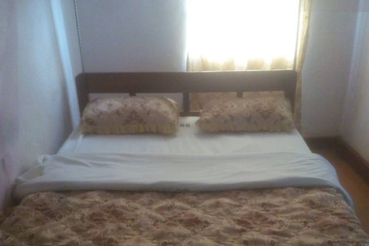 A bed with a patterned bedspread and two pillows, a window with curtains, and a plain wall.