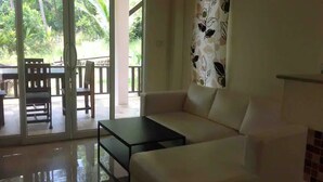 Un salon comprenant un canapé, une table basse et une porte-fenêtre coulissante donnant sur un espace extérieur avec une table et des chaises.