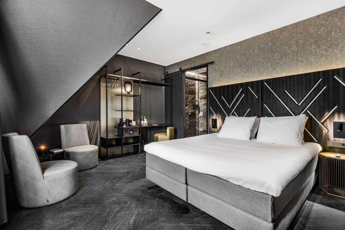 Une chambre moderne avec un grand lit, un coin salon avec un fauteuil, un bureau et une armoire.