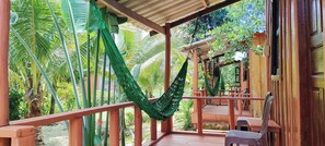 Eine hölzerne Veranda mit einer Hängematte, umgeben von üppiger tropischer Vegetation.