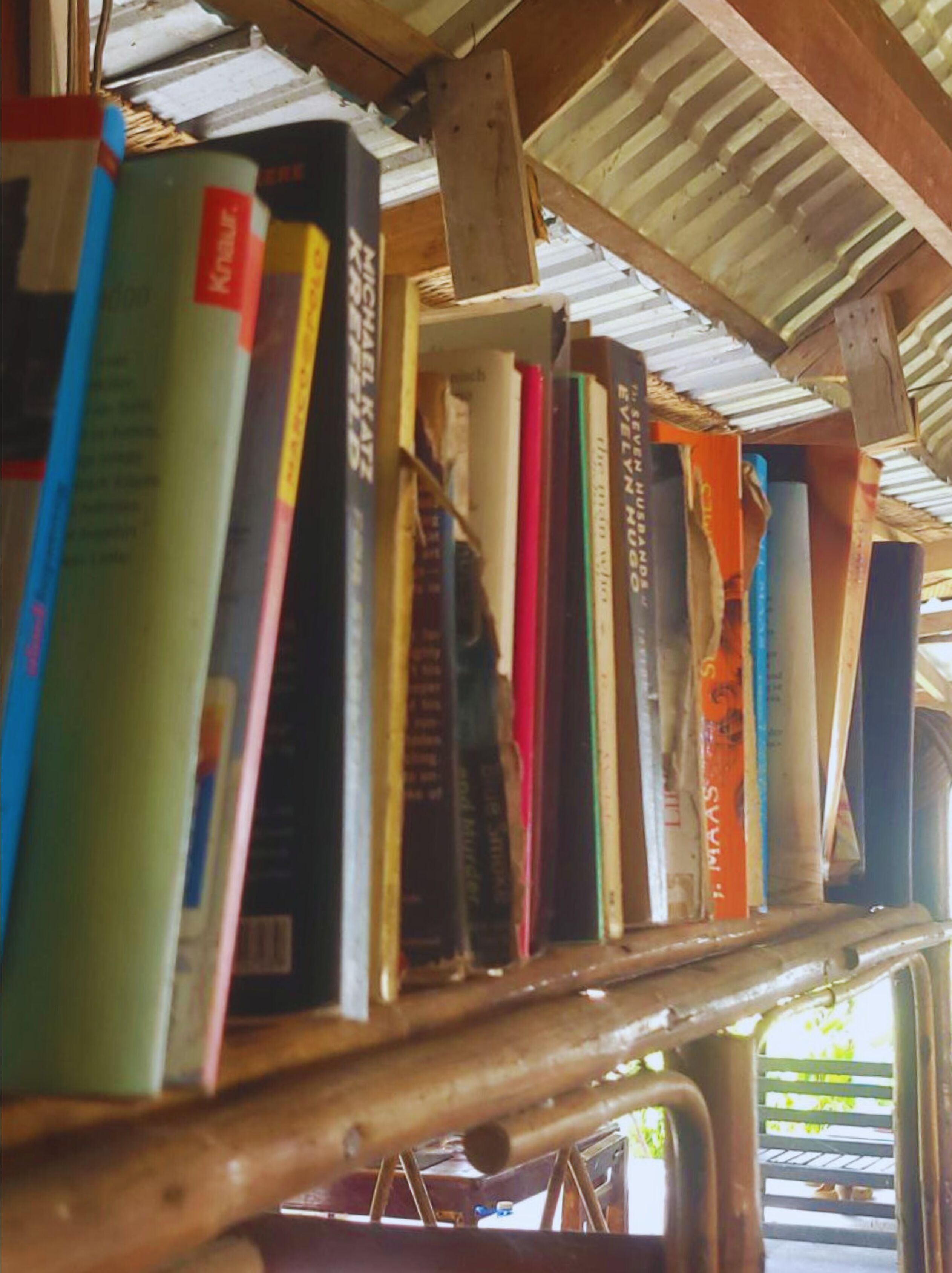 A collection of books on a shelf under a corrugated metal roof.