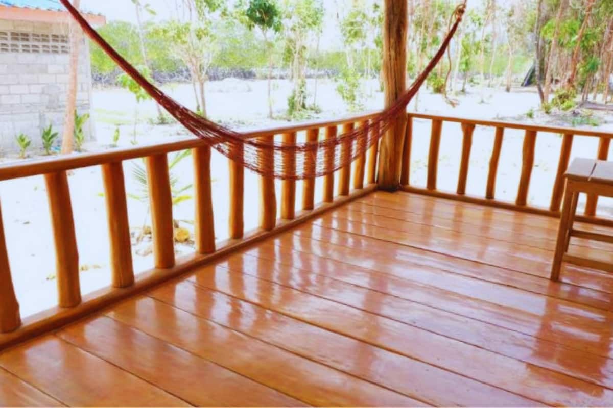 A wooden deck with a hammock, wooden railing, and a view of greenery.