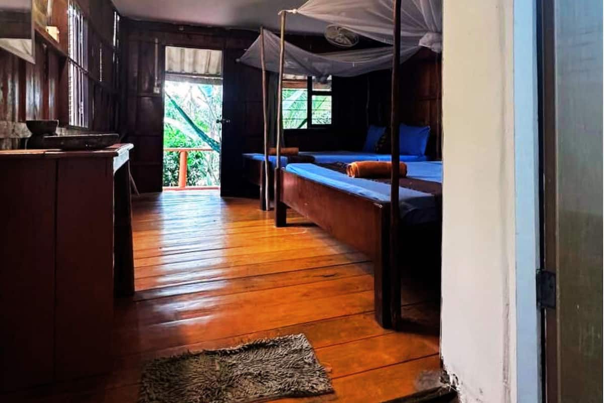 A room with a wooden floor, a kitchen area, and a bed with a canopy.