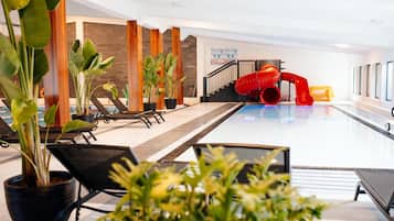 Zona de piscina con sillas de descanso, plantas en macetas y un tobogán rojo.