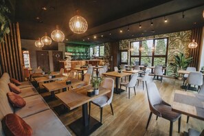 Un restaurant amb taules i cadires de fusta, zona de bar i grans finestres amb vista a vegetació.