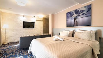 Habitación de hotel con una cama, un televisor instalado en una pared de ladrillo, un ventanal grande y un cuadro de un paisaje marino.