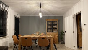 Una zona de menjador amb una taula de fusta, sis cadires, un moble amb portes de vidre i un llum penjant.