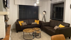 Un saló modern amb un sofà modular, dues taules de centre de fusta, una làmpada de peu i un televisor fixat a la paret.