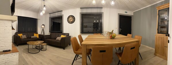 Ein modernes Wohnzimmer mit Sofa, Couchtisch, Esstisch und Stühlen. An der Wand hängt eine Uhr und es gibt einen Schrank mit Glastüren.