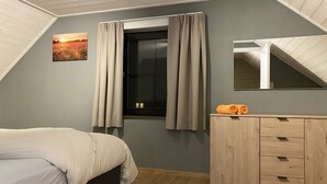 Un dormitori amb un llit, un taulell de fusta, una finestra amb cortines i un quadre a la paret.