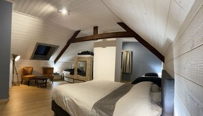 Ein Schlafzimmer mit schrägem Dach, einem Bett, einem Sessel, einem Schreibtisch und einem Fenster.