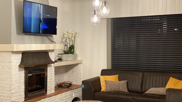 Un saló modern amb una llar de foc, un televisió de pantalla plana penjada a la paret, un sofà amb coixins i una taula de centre.