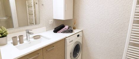 A modern bathroom with a built-in washing machine, a sink, and a towel rack.
