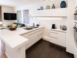 Une cuisine moderne avec des meubles blancs, un îlot central intégré et un téléviseur à écran plat fixé au-dessus de l’îlot.