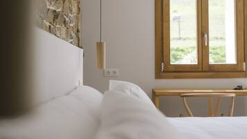 A bedroom with a stone wall, a wooden headboard, a wooden nightstand, and a window with a view of greenery.