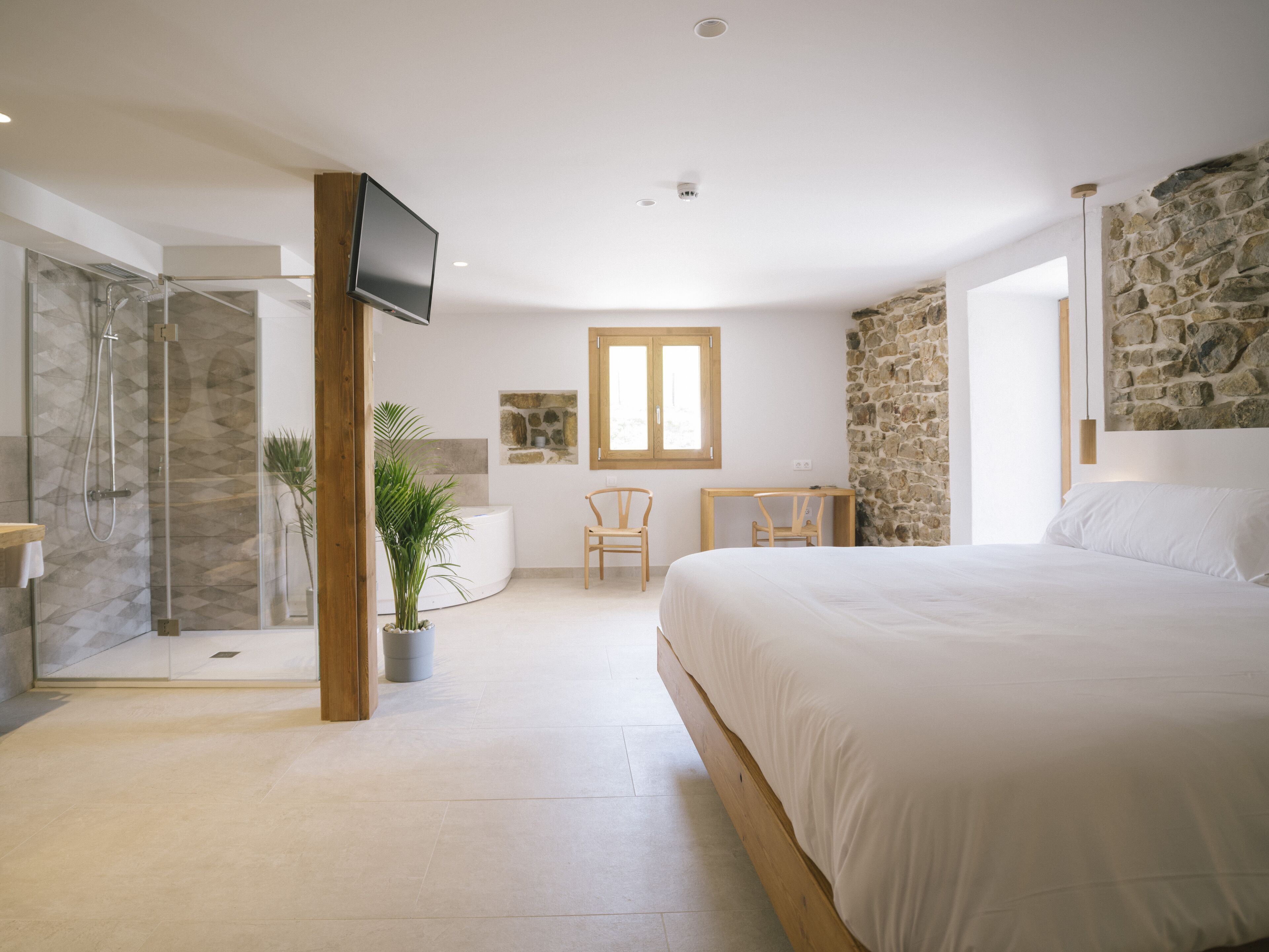 A bedroom with a large bed, a shower, a desk, and a TV.