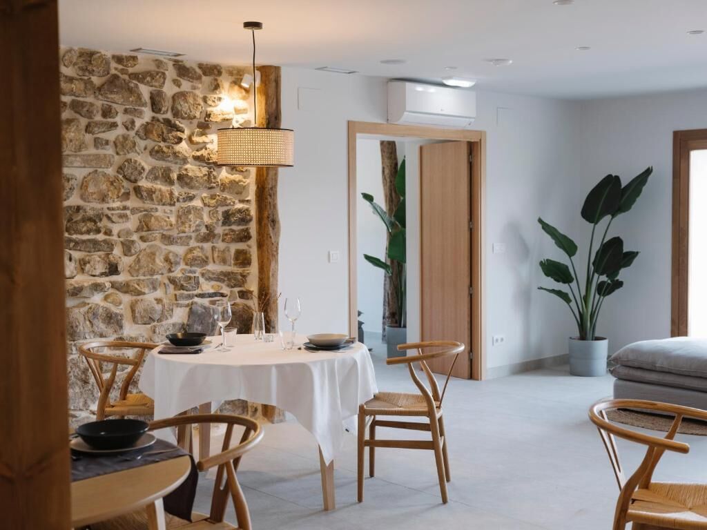 Un coin repas avec un mur en pierre, des chaises en bois, une table ronde et un luminaire suspendu.