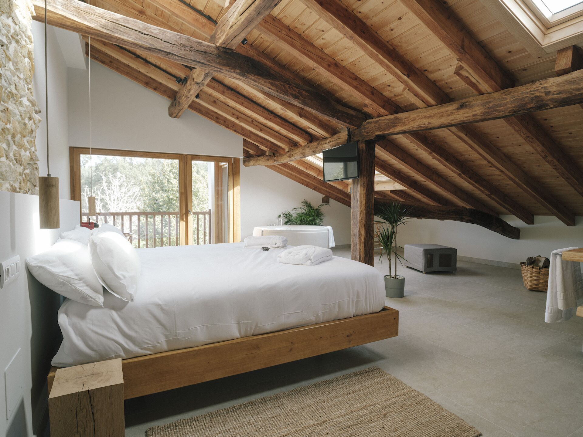 Un dormitorio con techo de madera, una cama con ropa de cama blanca, una ventana y una planta.
