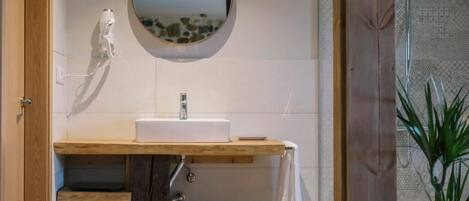 A bathroom with a wooden vanity, a round mirror, and a shower area.