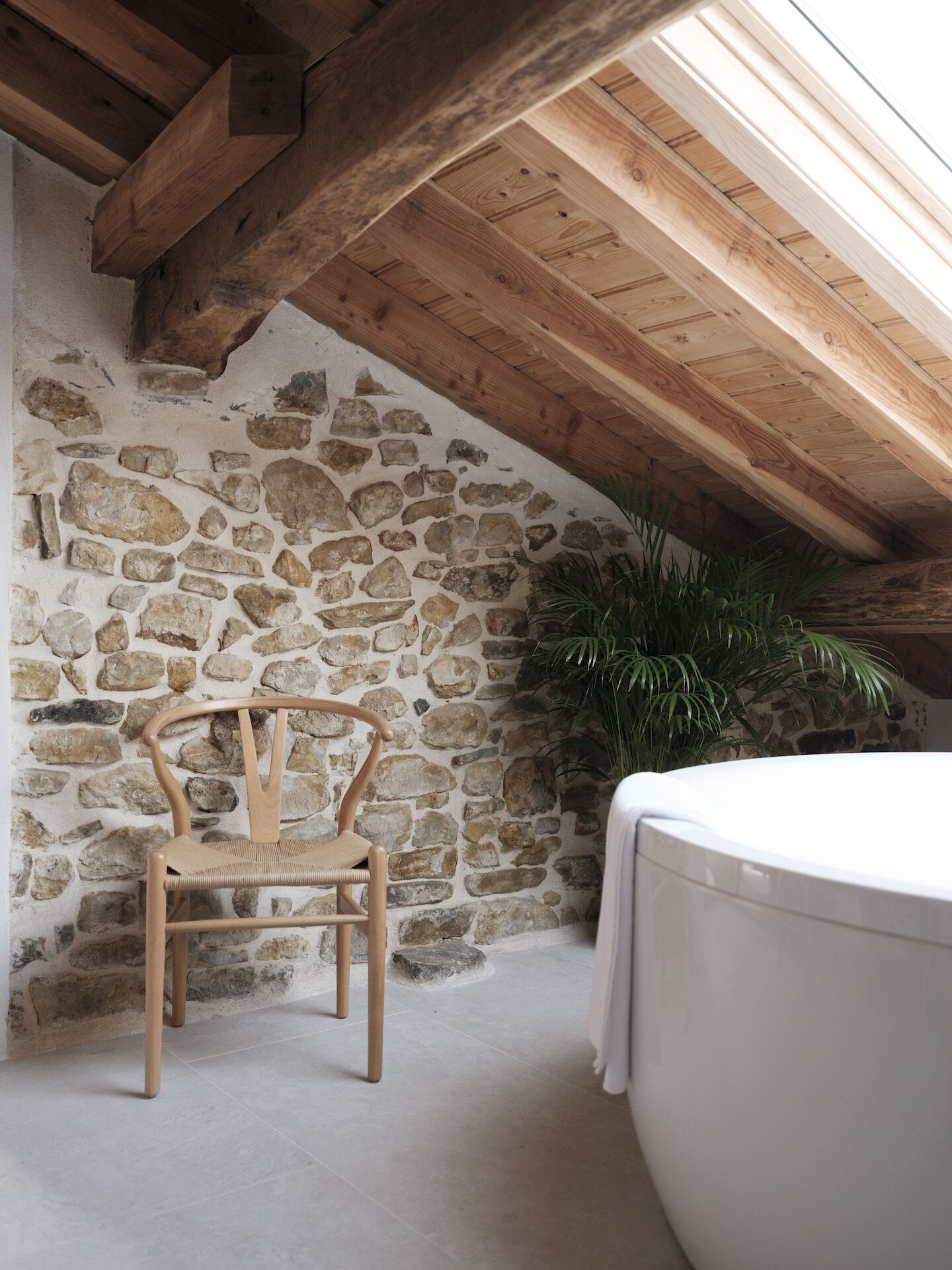 Pared de piedra con una silla de madera y una bañera en una habitación rústica con vigas de madera.