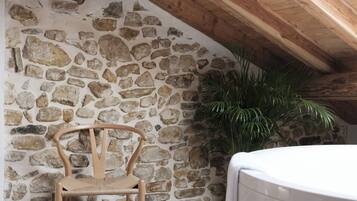 Pared de piedra con una silla de madera y una bañera en una habitación rústica con vigas de madera.