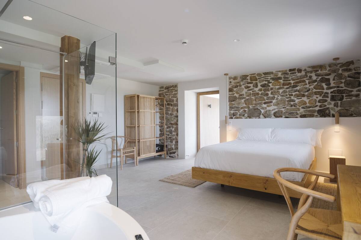 Ein modernes Schlafzimmer mit Steinwand, Duschkabine aus Glas, hölzernem Bettgestell und weißem Sofa.