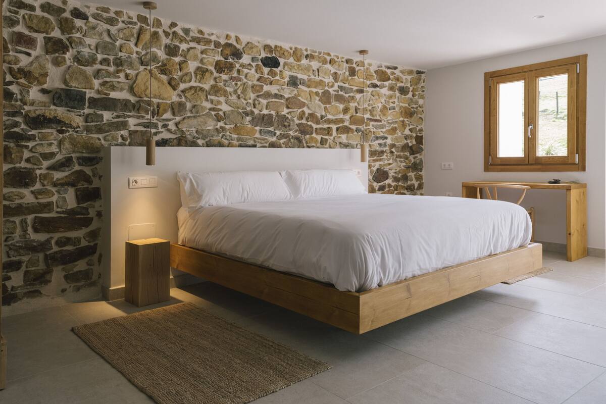 Ein Schlafzimmer mit Steinwand, hölzernem Bettgestell, Nachttisch und Fenster.